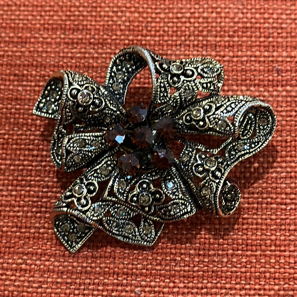 Gold tone brooch with brown rhinestones.  2” wide by 1.5” high.